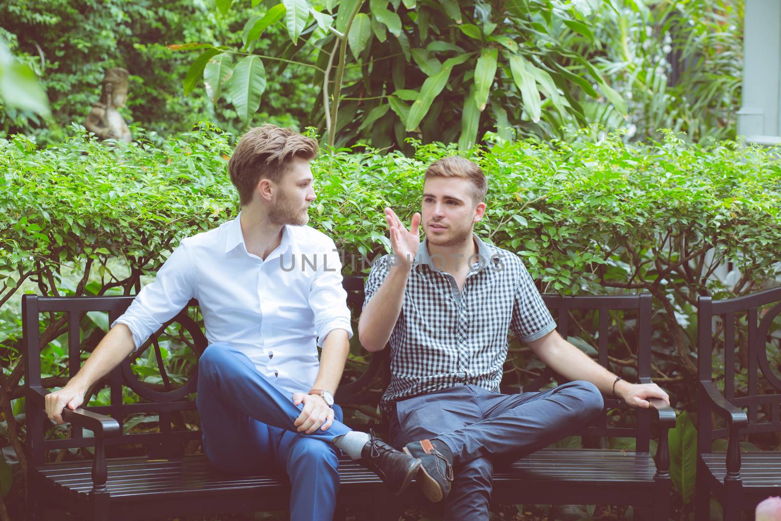Two friends men talking sitting in a garden.