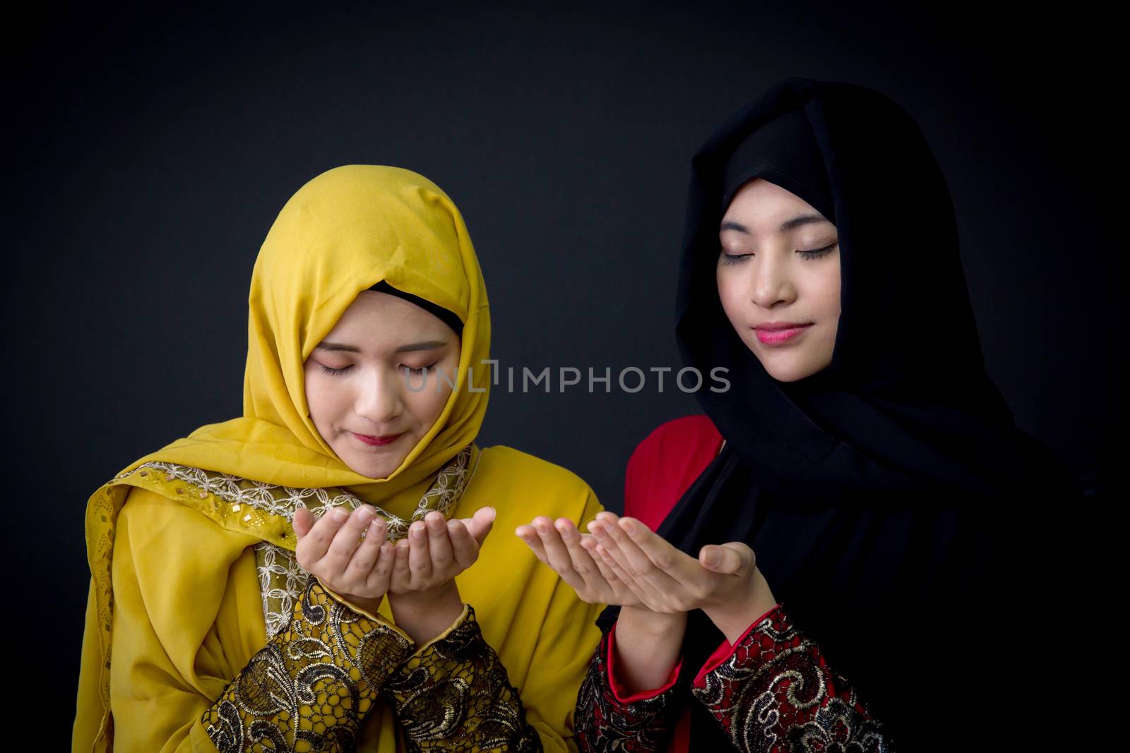 religious young Muslim two women praying over black background.