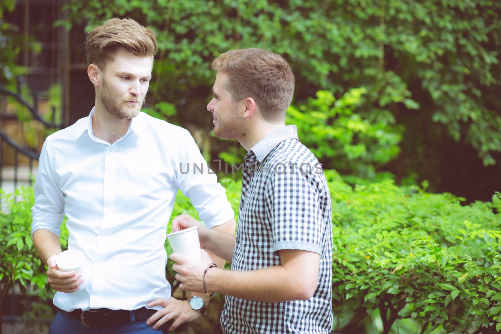 Two friends men talking standing in a garden. by nnudoo