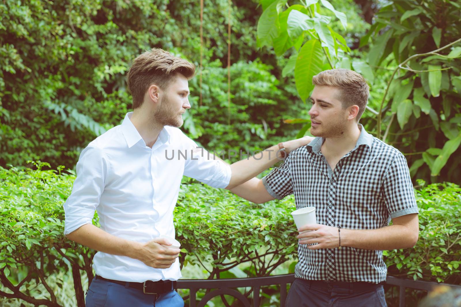 Two friends men talking standing in a garden.