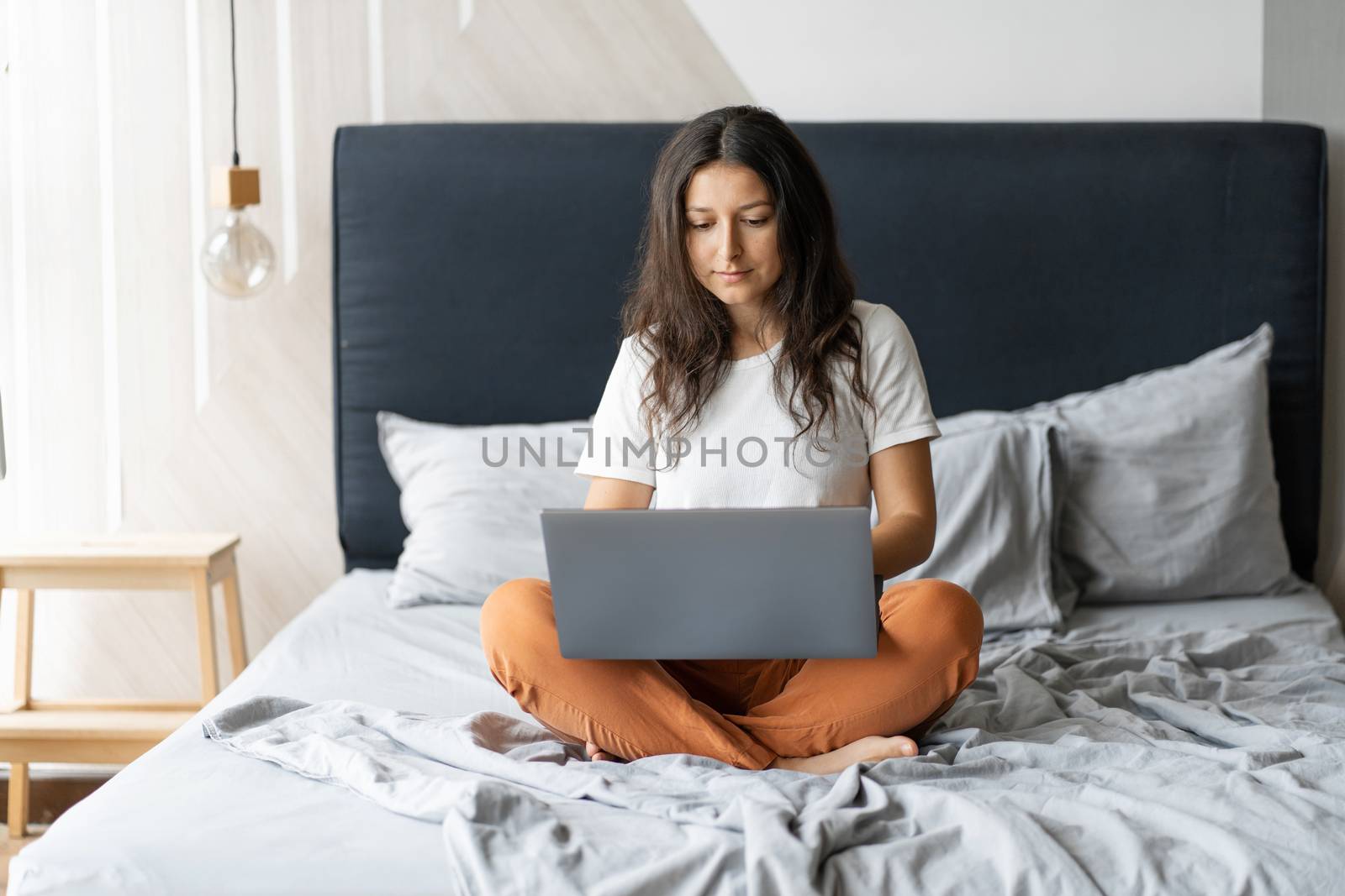 Beautiful young brunette girl with a laptop sitting on the bed. Stylish modern interior. A cozy workplace. Shopping on the Internet by Try_my_best
