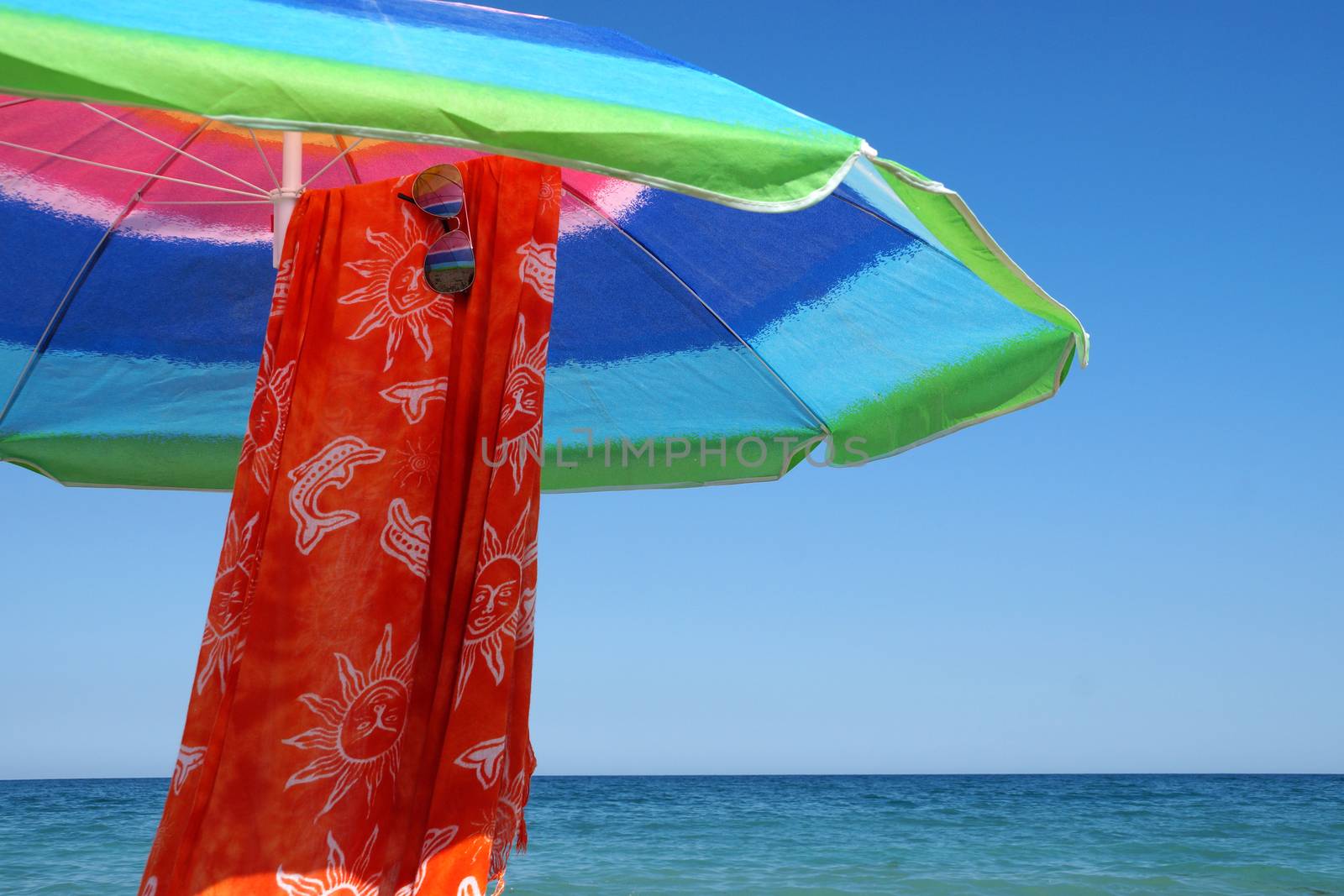 beach umbrella, pareo and sunglasses against the sea horizon and clear sky, copy space.