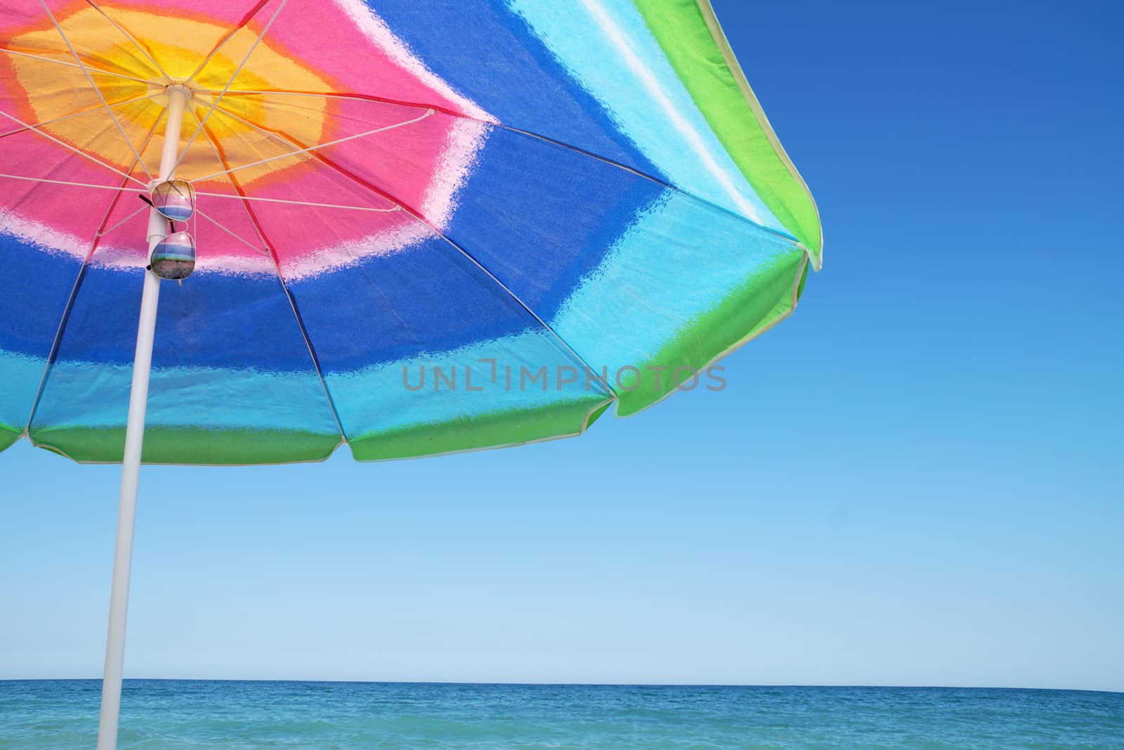 beach umbrella, pareo and sunglasses against the sea horizon and clear sky, copy space