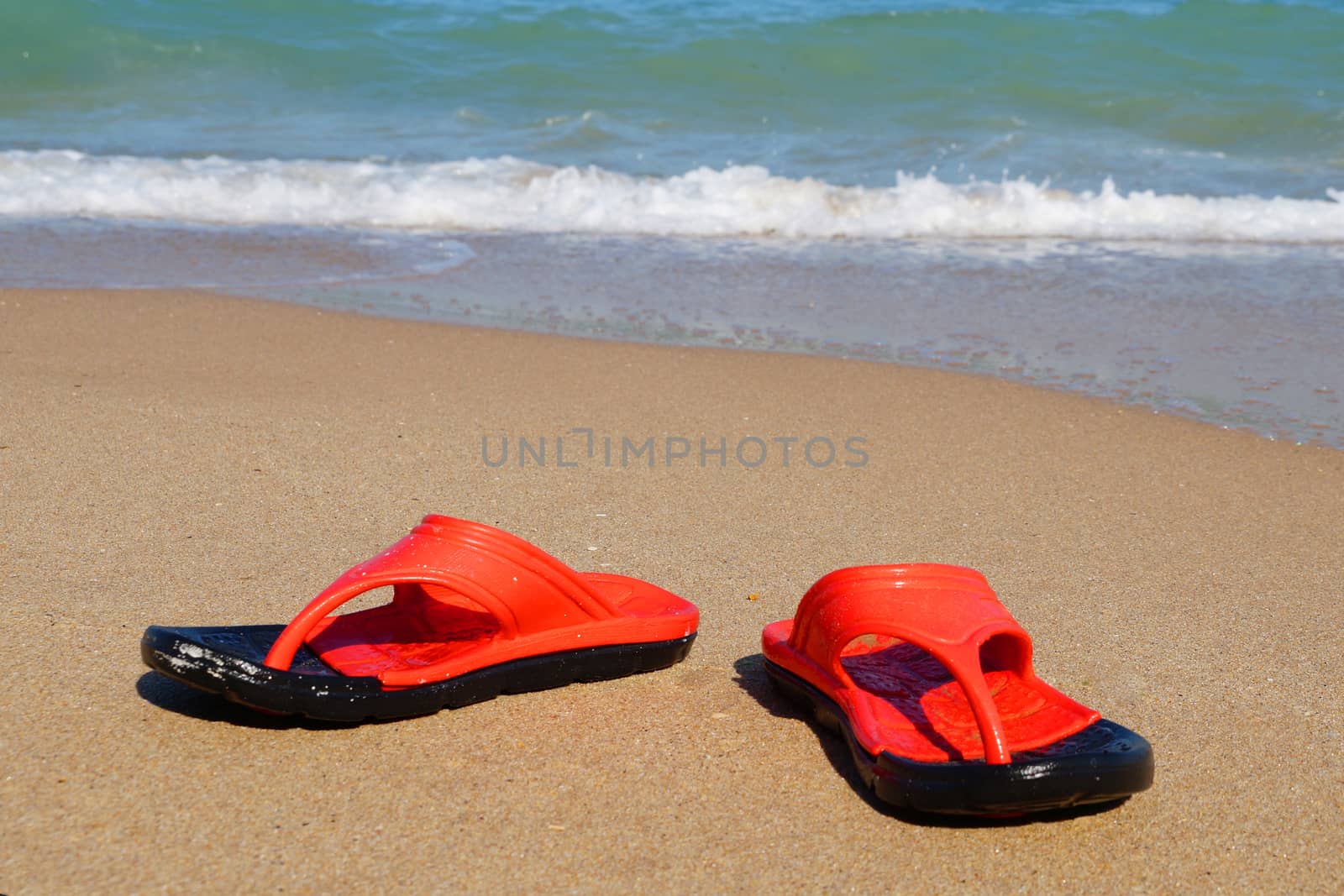 red beach slates on an empty sandy beach near the sea waves