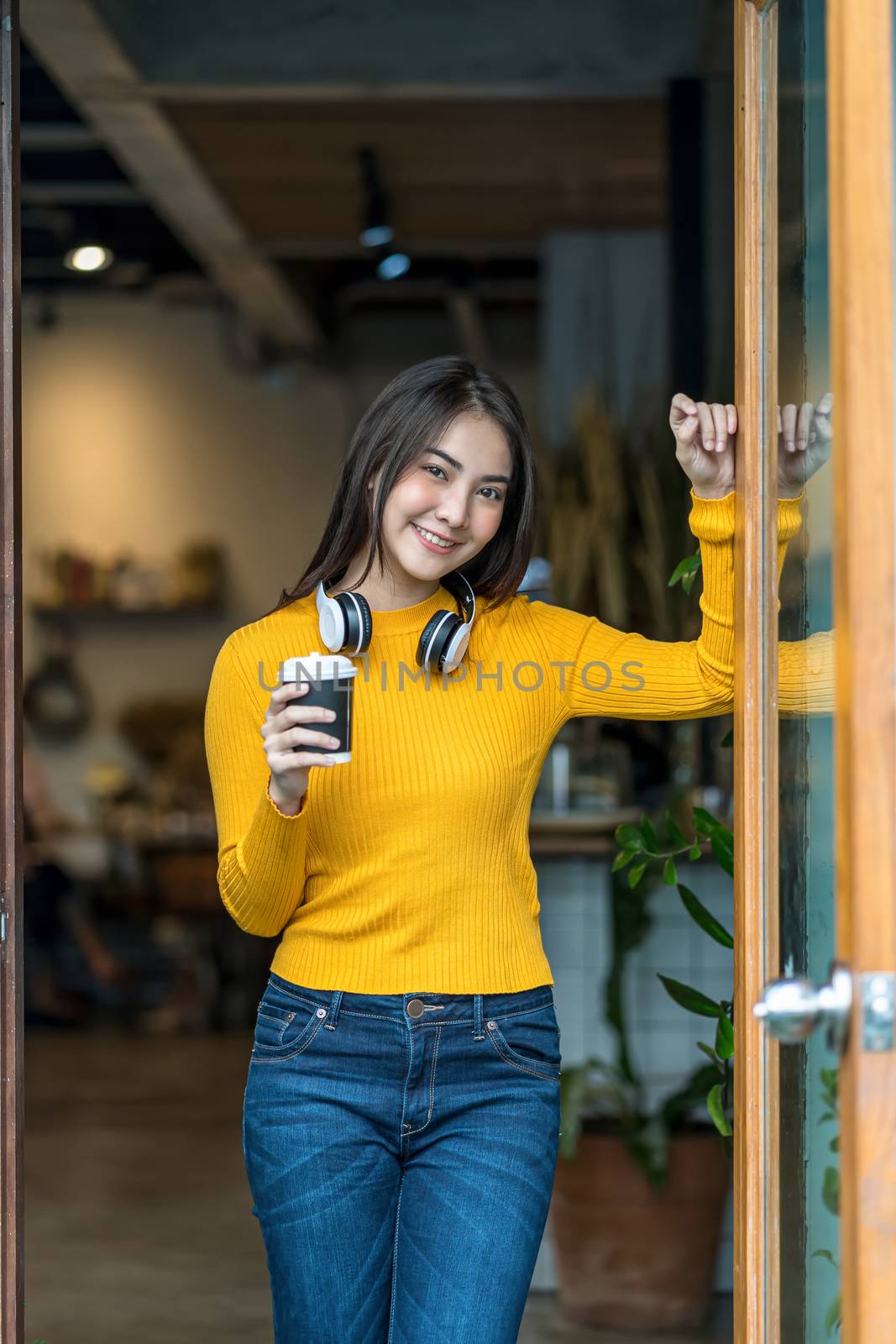 Asian young female holding a cup of coffee in modern coffee shop by Tzido