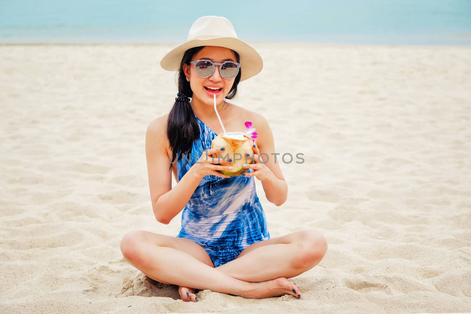 Happy woman with fresh coconut water on the beach by Surasak