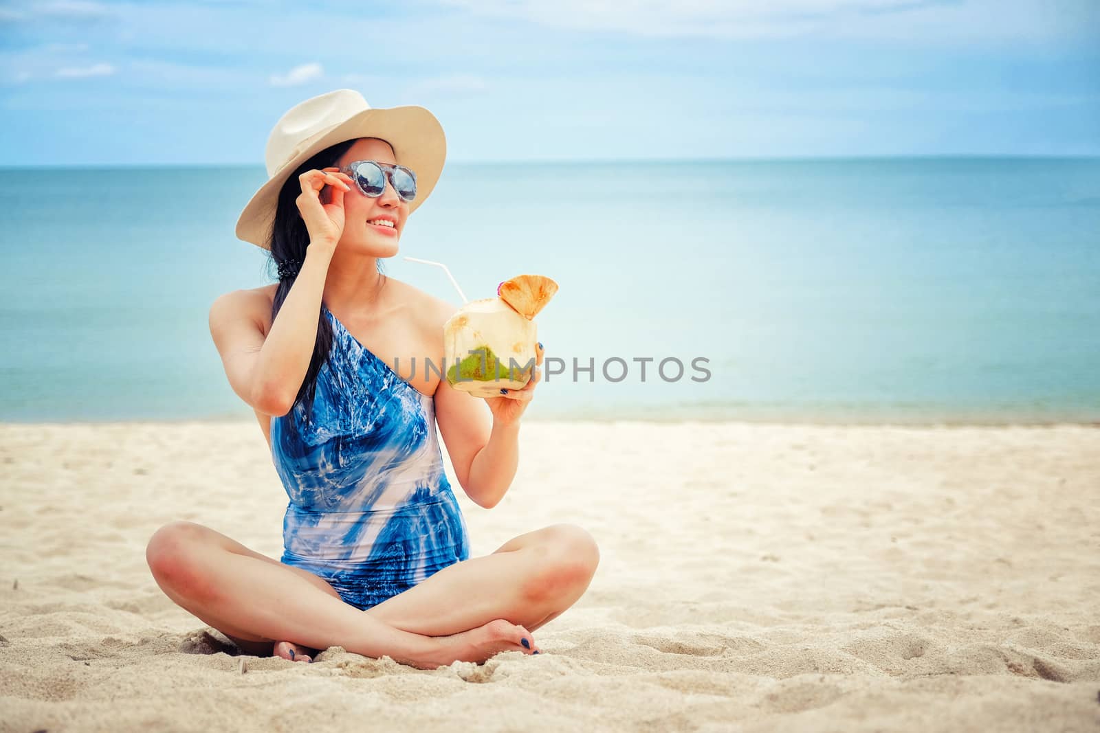 Happy woman with fresh coconut water on the beach by Surasak