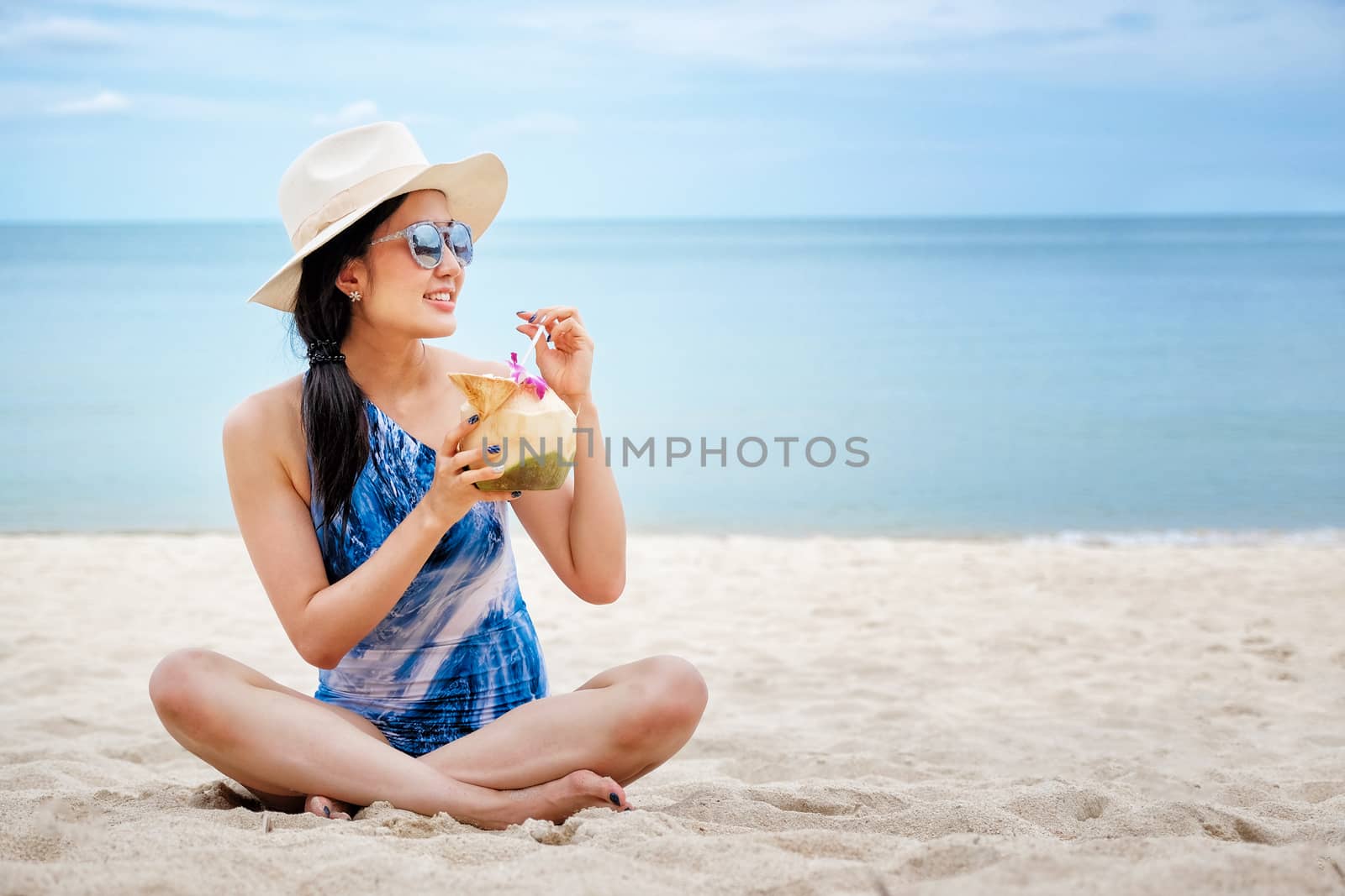Happy woman with fresh coconut water on the beach by Surasak