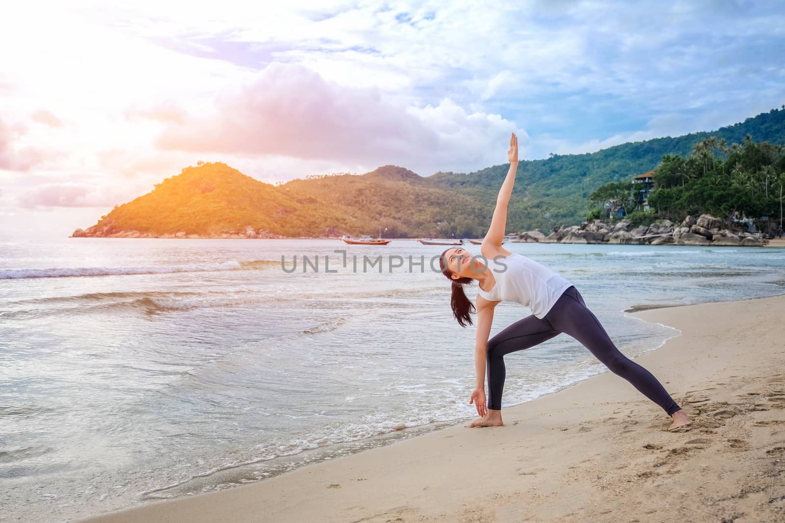 Young beautiful woman practicing yoga on the beach at sunrise