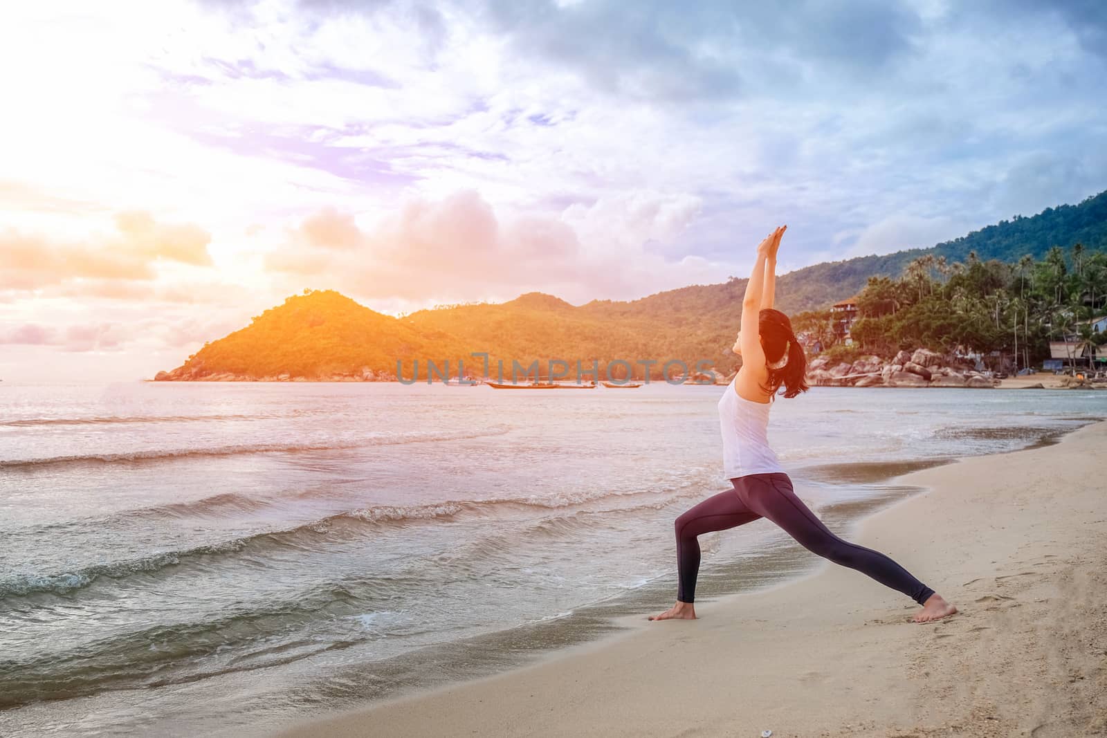 Young beautiful woman practicing yoga on the beach at sunrise