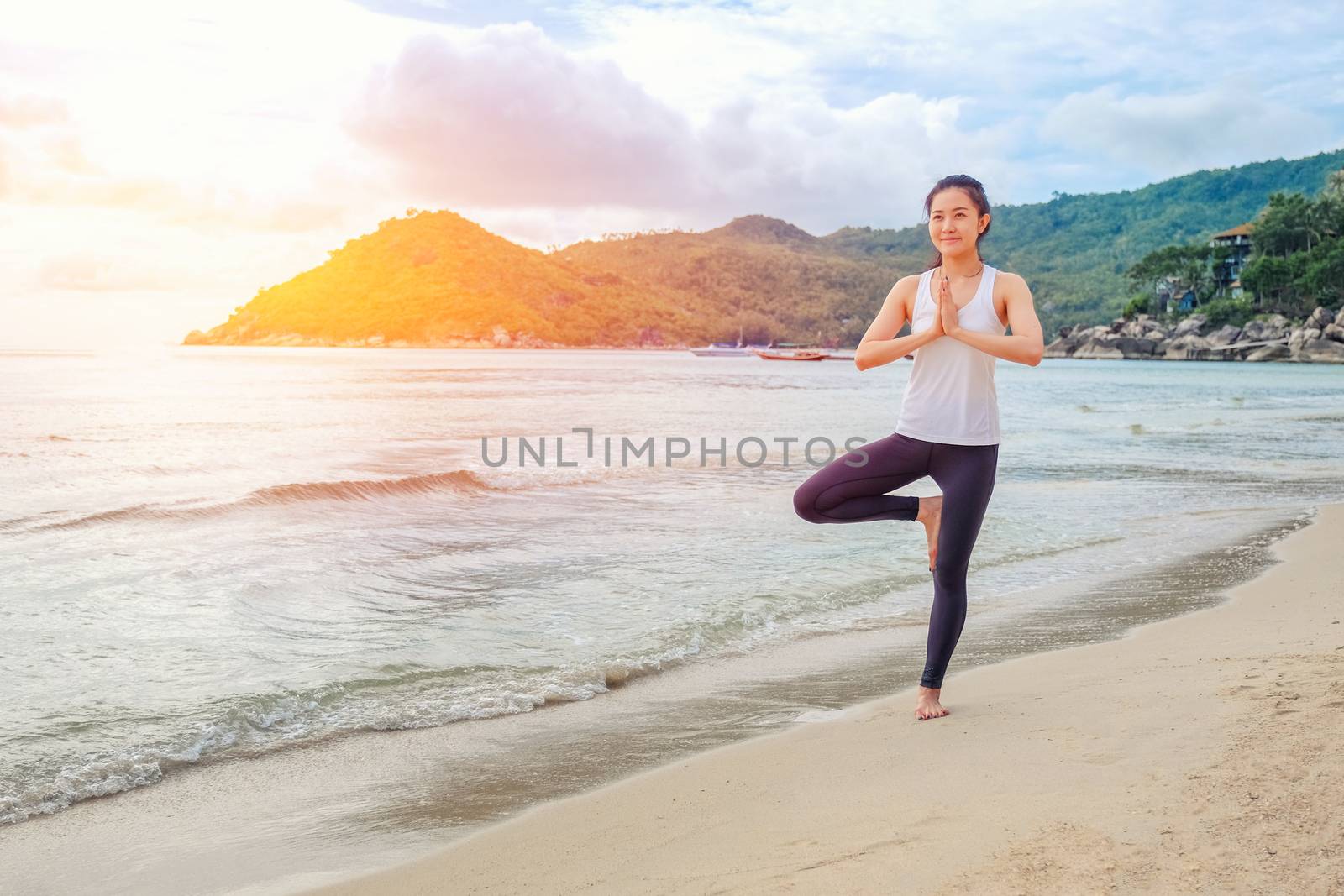 Young beautiful woman practicing yoga on the beach at sunlight by Surasak