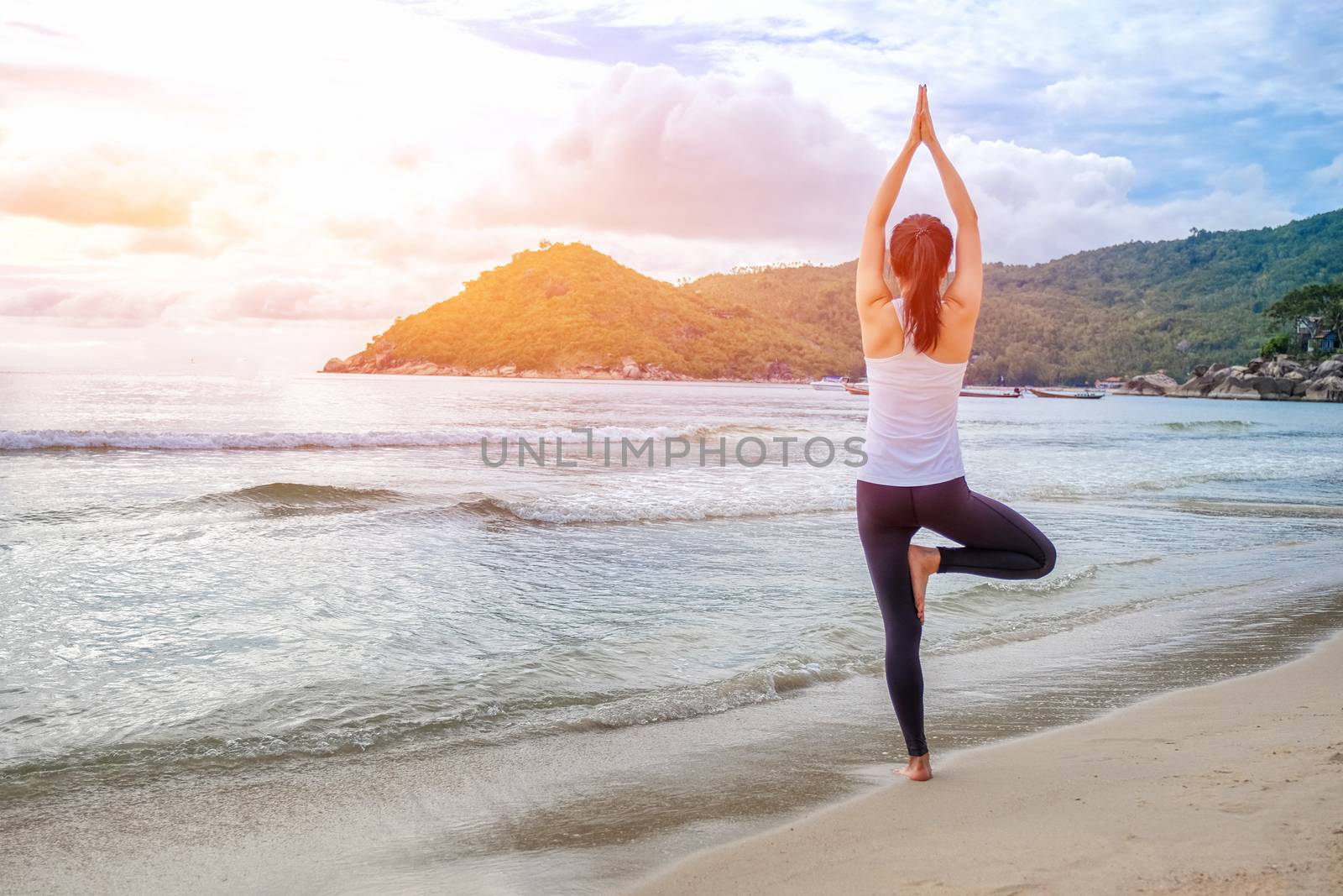 Young beautiful woman practicing yoga on the beach at sunrise by Surasak