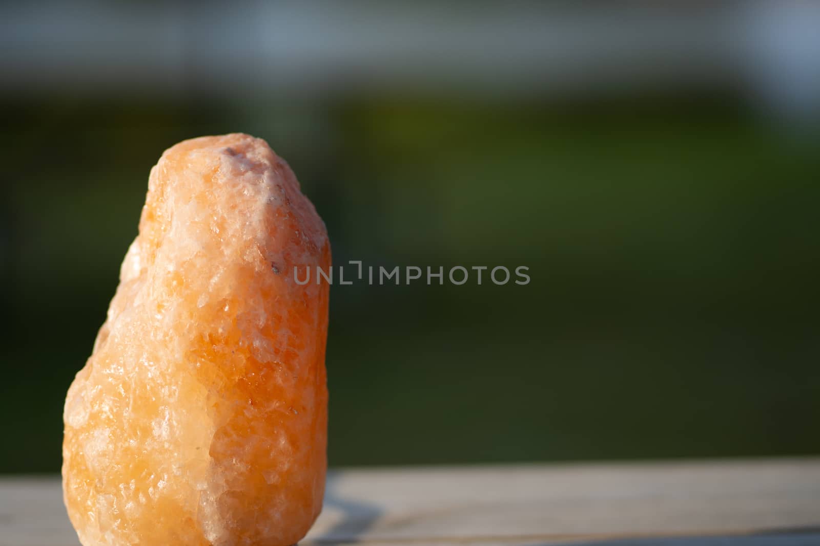 Blurred outdoor background with a closeup of a himalayan salt rock on a wood table in the summer sunlight