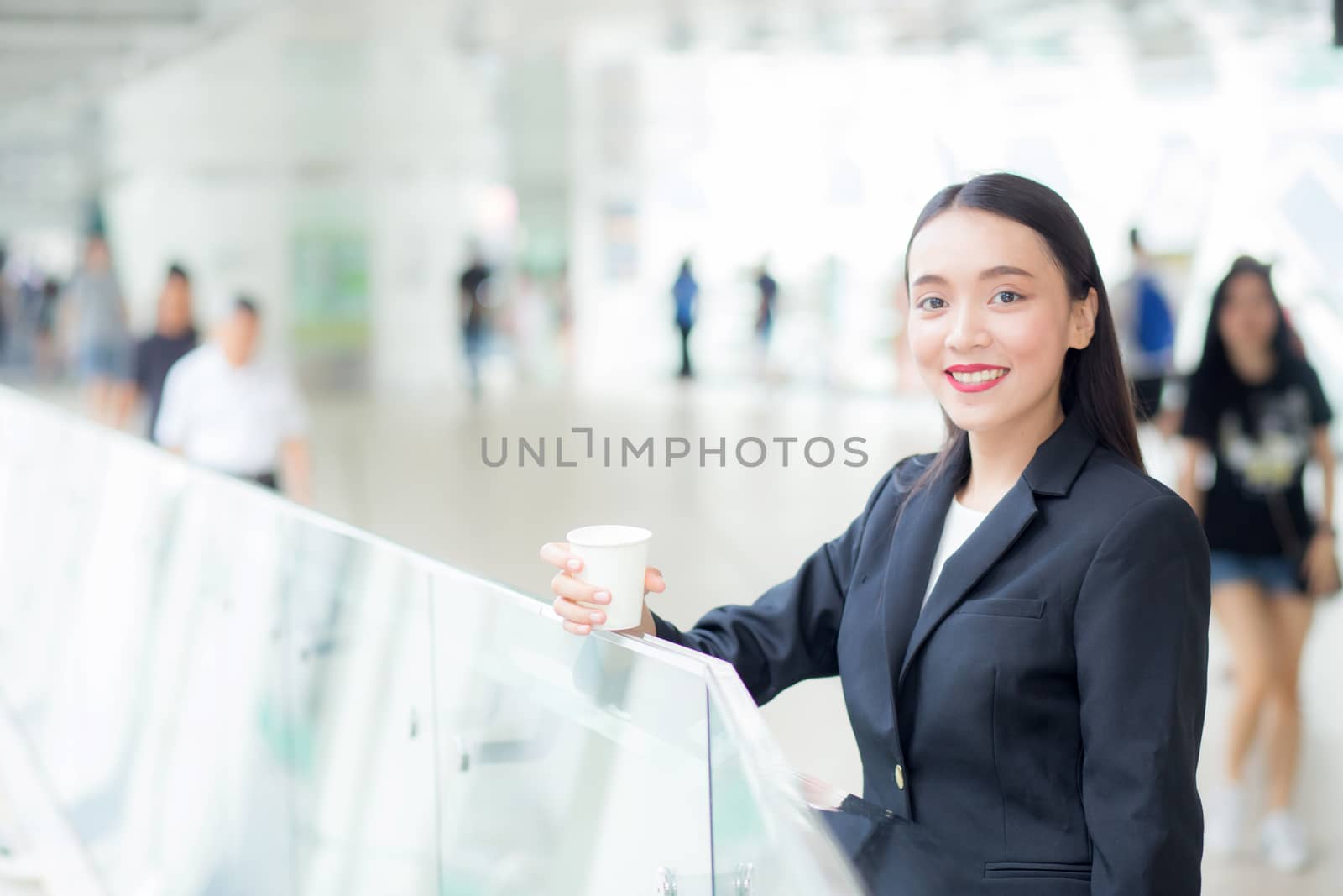 Asian businesswoman talking mobile phone and holding a coffee cup against urban scene, business concept.