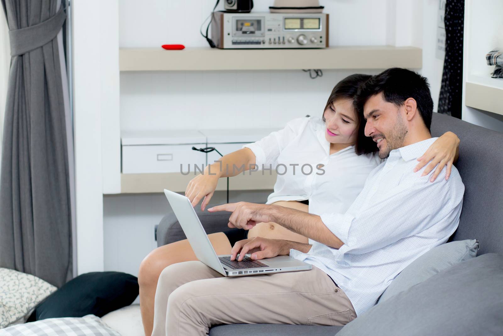 Portrait of a asian young couple husband and wife sitting on the sofa while using notebook computer in living room.