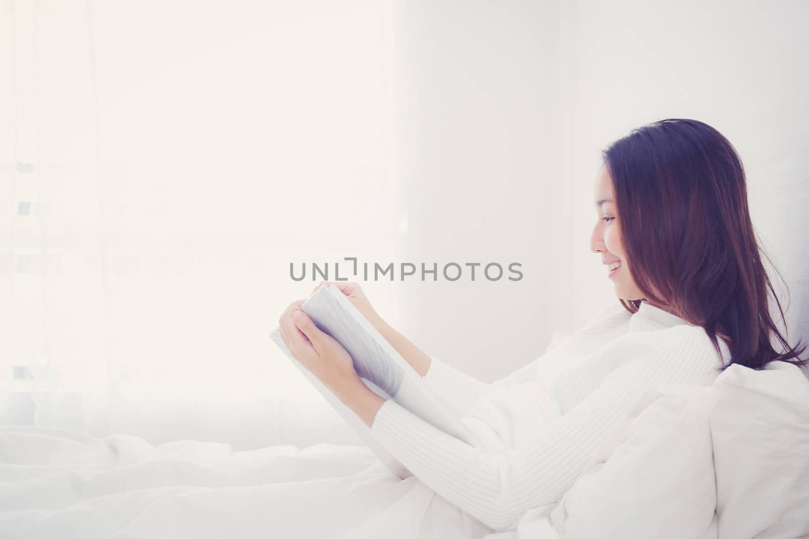 Asian woman reading a book and smiling in bedroom. lifestyle con by nnudoo