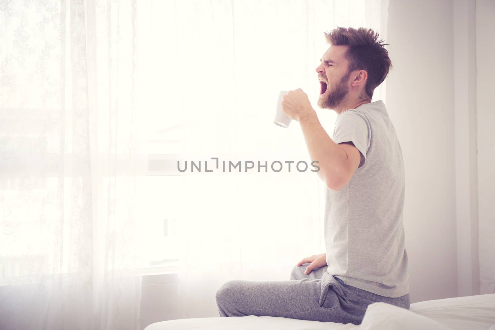 Lifestyle portrait of bedroom concept: Man holding a cup of coffee and yawn with on bedroom good morning,