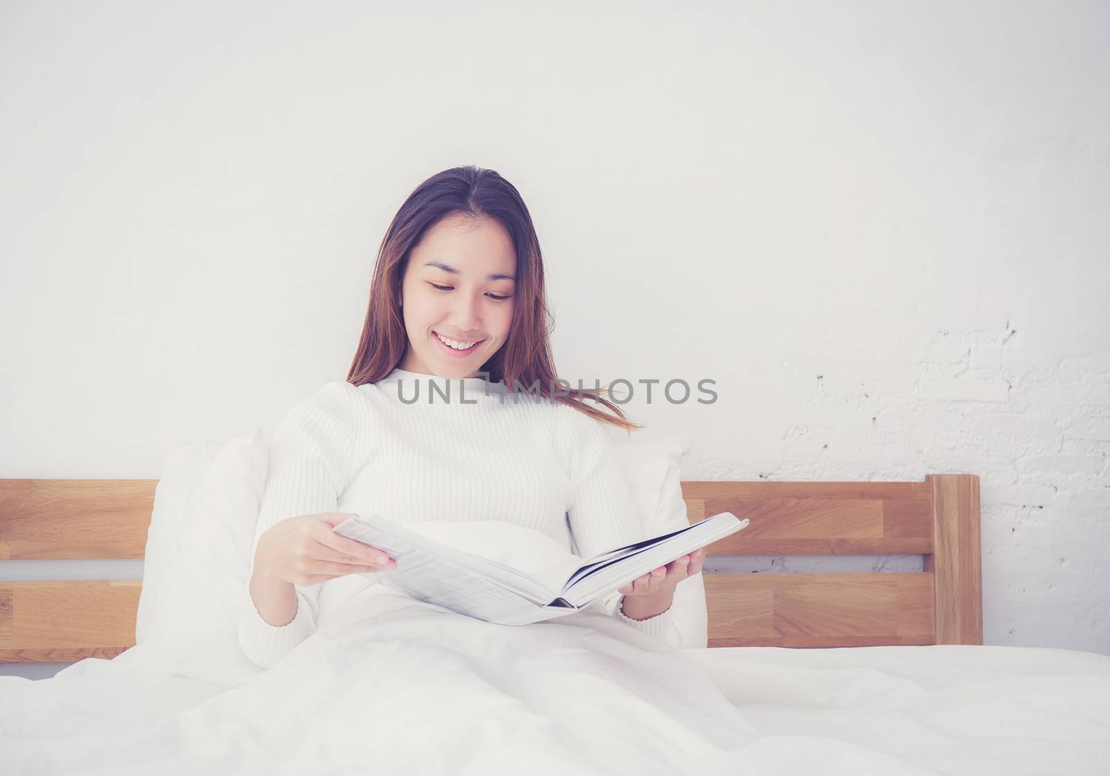Asian woman reading a book and smiling in bedroom. lifestyle concept.