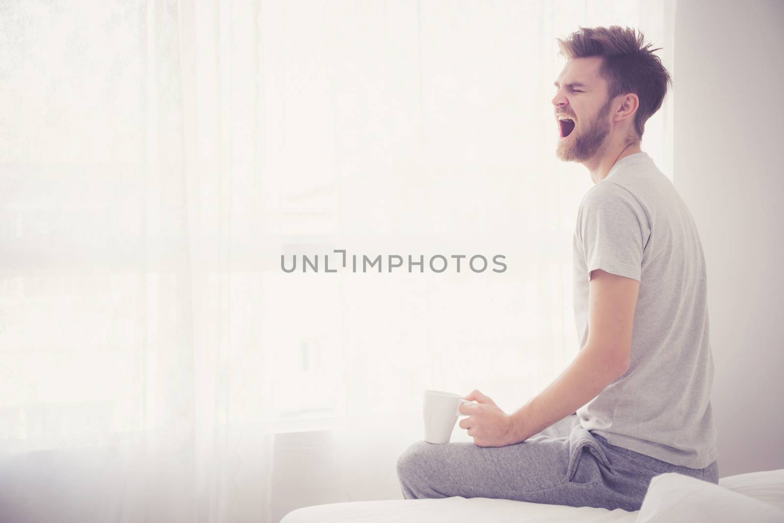 Lifestyle portrait of bedroom concept: Man holding a cup of coffee and yawn with on bedroom good morning.