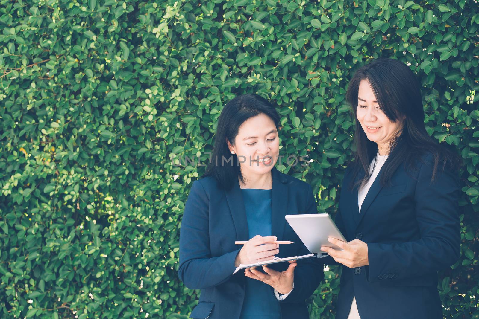 Two business people discussing information on a tablet-and taking notes as they work together as a team in the garden.