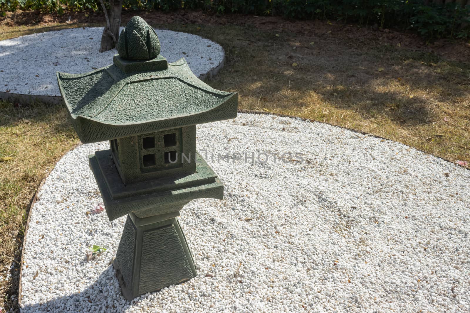 Stone or Rock Japanese Pagoda Lantern in Garden with Small White Rock on Ground on Left Frame with Natural Light