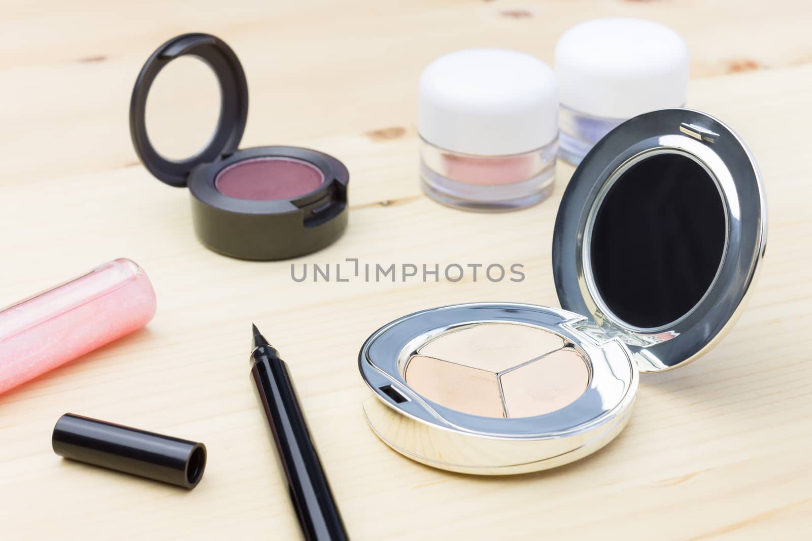 Woman cosmetics include eyes liner and lip gloss, and eyeshadow and foundation or face powder on wood table