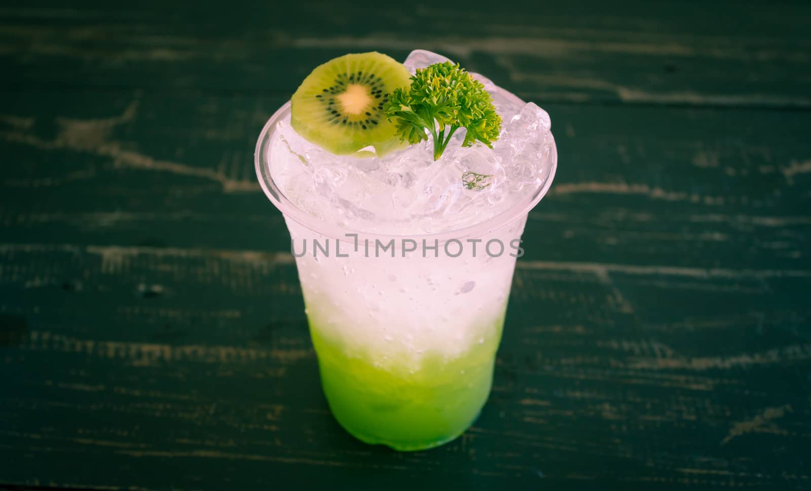 Green Italian Soda Cold Beverage and Kiwi Fruit and Parsley Center. Green Italian Soda Cold Beverage with Kiwi fruit and ice in glass on wood table for food and drink category