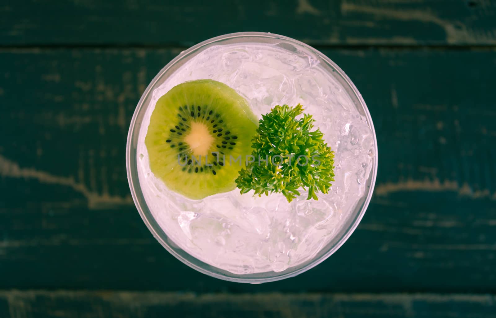 Green Italian Soda Cold Beverage and Kiwi Fruit and Parsley. Green Italian Soda Cold Beverage with Kiwi fruit and ice in glass on wood table. Green Italian Soda with Kiwi for food 
and drink category