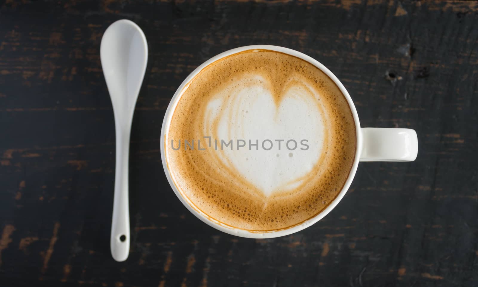 Heart Shape Froth Milk Latte Art in White Coffee Cup and Spoon on Black Wood Table. Heart shape froth milk Latte art hot beverage for coffee lover
