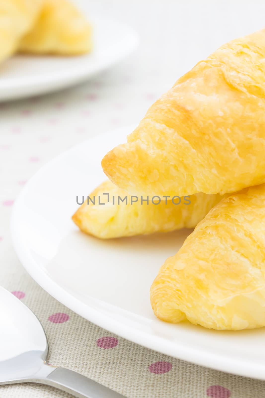 Croissant or Bread on White Dish on Placemat with Spoon Close up by steafpong