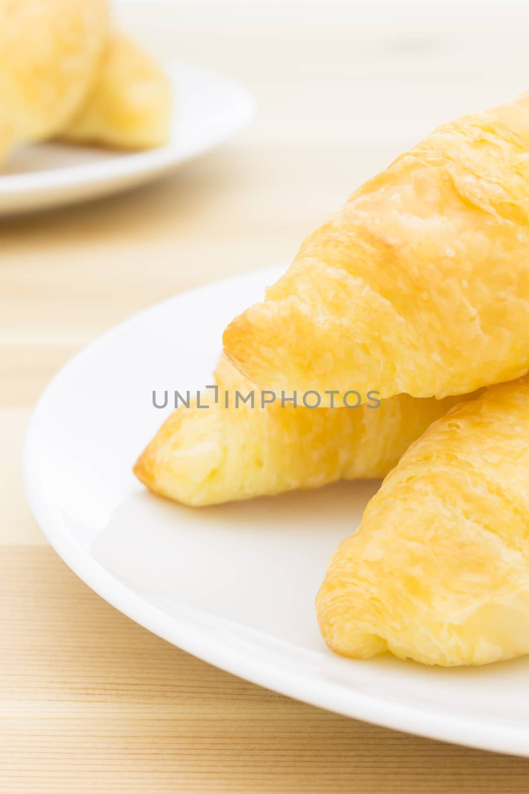 Croissant or Bread on White Dish on Wood Table Portrait View by steafpong