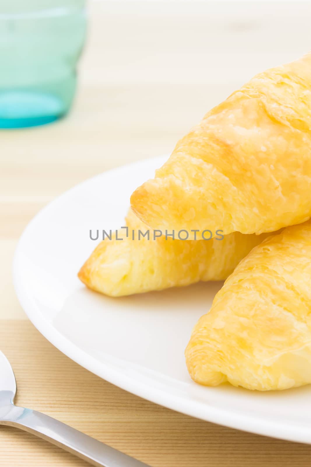 Croissant or Bread on White Dish on Wood Table with Spoon and Gl by steafpong