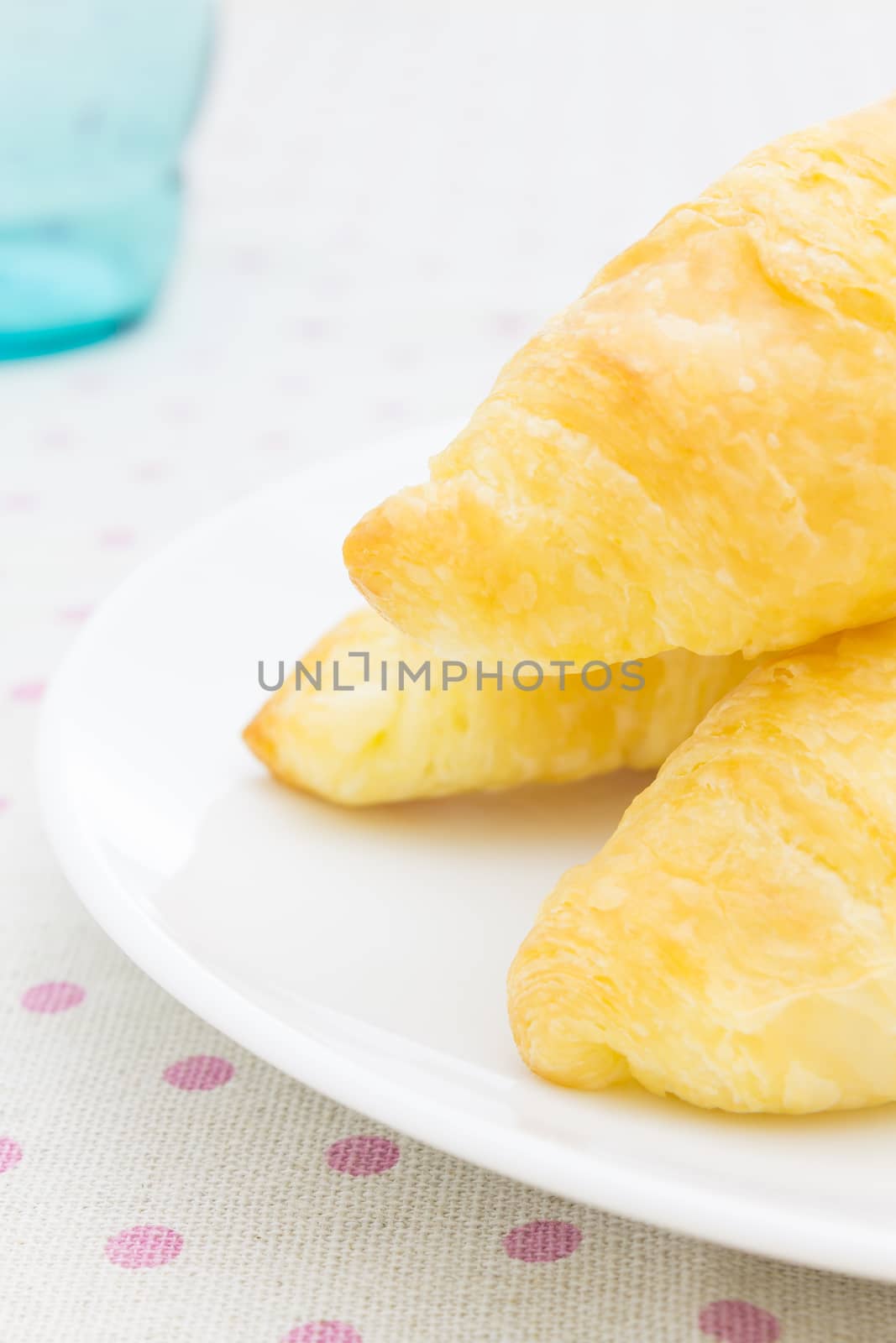Croissant or bread or bakery on white dish on pink point placemat with glass close up view