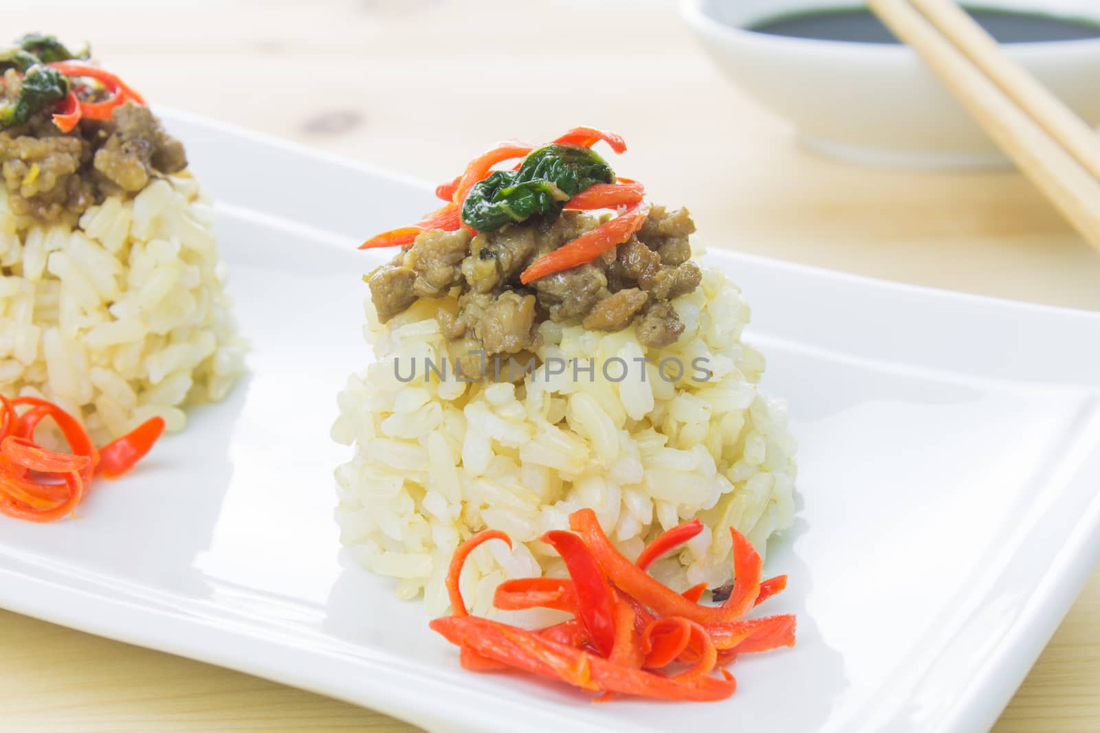 Salted pork with chili & Basil leaves close up view on white rectangle dish. Thai food on wood table.