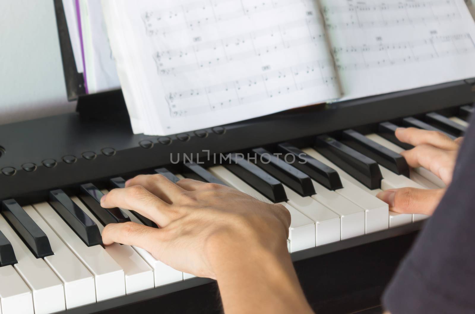 Hand of Piano Player on White Keys and Black Keys of Electric Piano with Piano Staff or Sheet Music