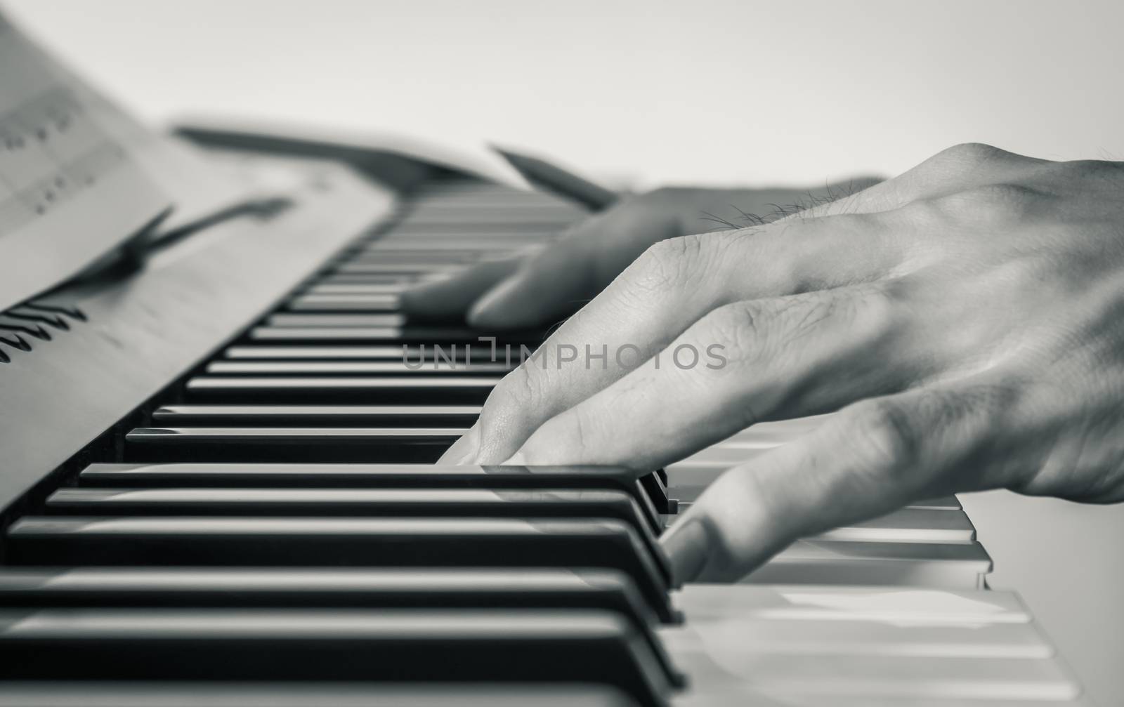 Hand of Piano Player on White Keys and Black Keys of Electric Piano with Sheet Music or Piano Staff