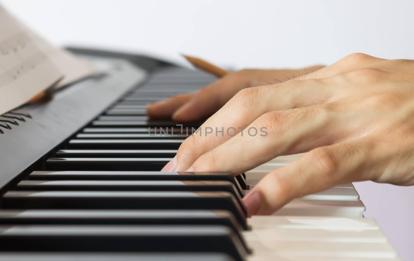 Hand of Piano Player on White Keys and Black Keys of Electric Piano with Sheet Music or Piano Staff