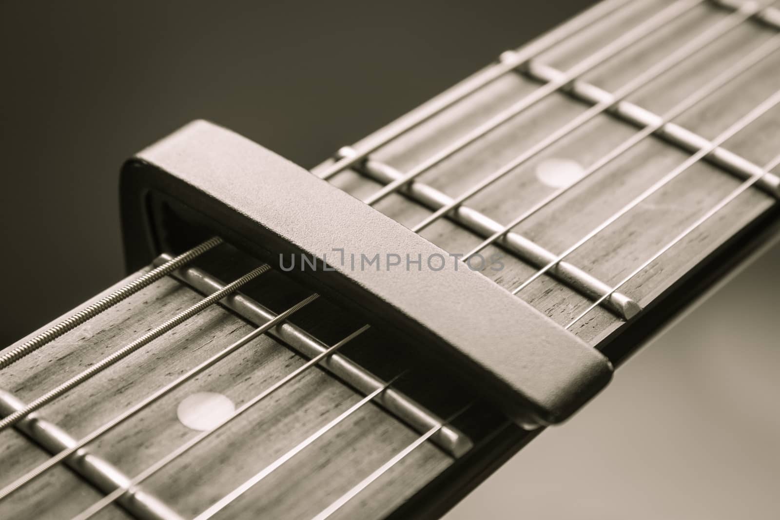 Black Capo on Acoustic Guitar String and Fingerboard with Soft Natural Light in Close up View