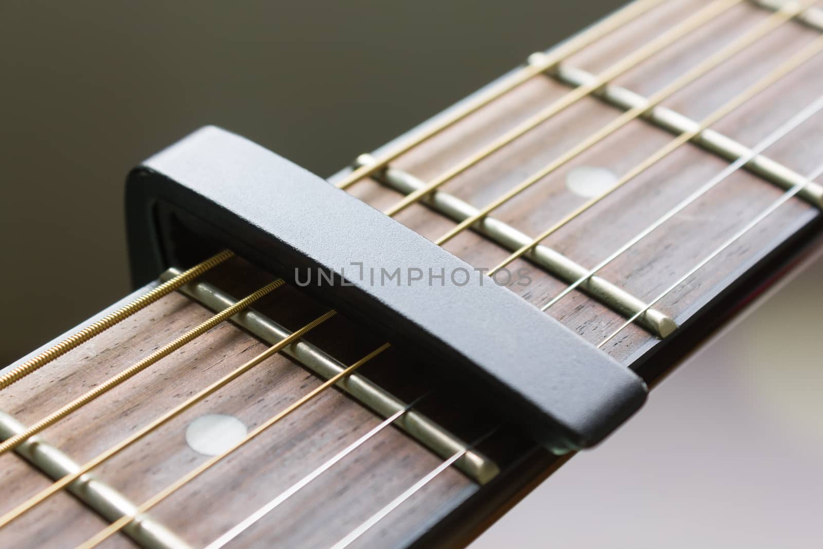 Black Capo on Acoustic Guitar String and Fingerboard with Soft Natural Light in Close up View