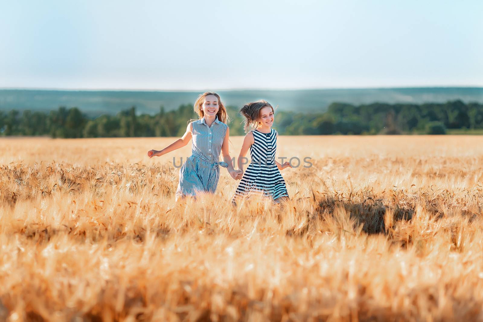 Happy teenage girls running down wheat field at the sunset