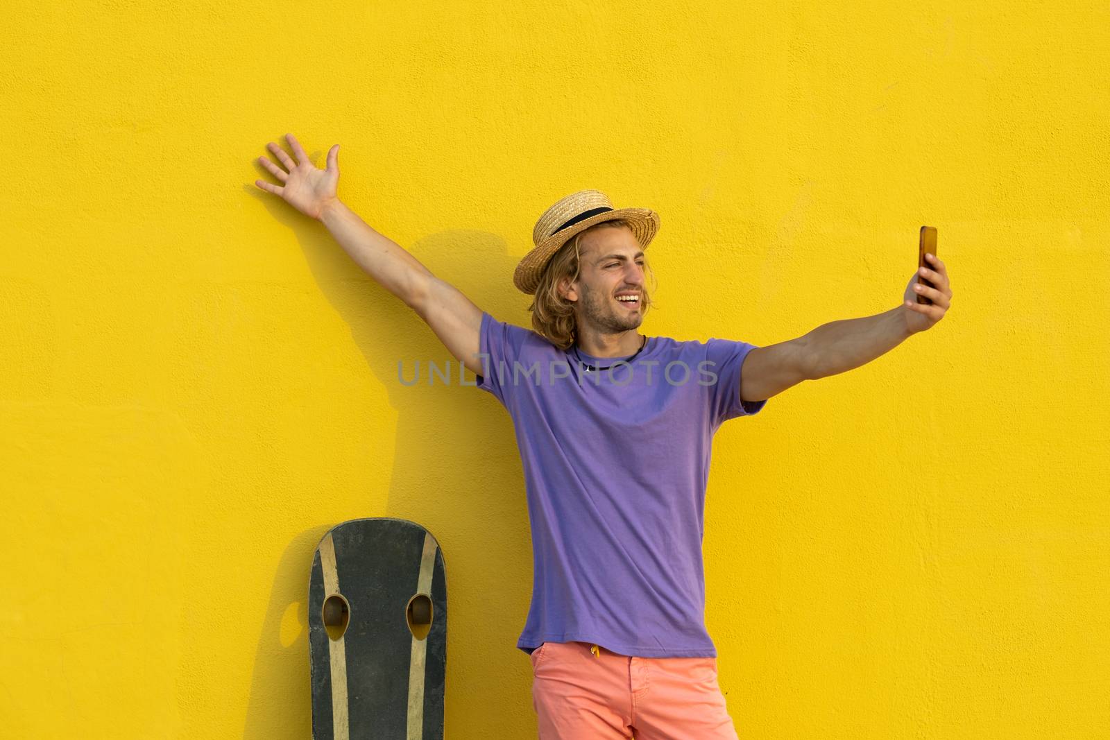 Young blond man with summer clothes, hat and sunglasses enjoying the summer and talking with the mobile phone