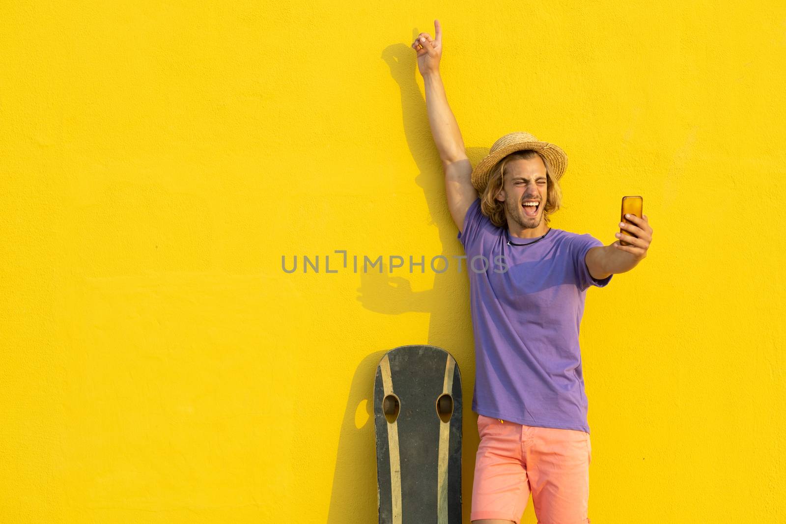 Young blond man with summer clothes, hat and sunglasses enjoying the summer and talking with the mobile phone