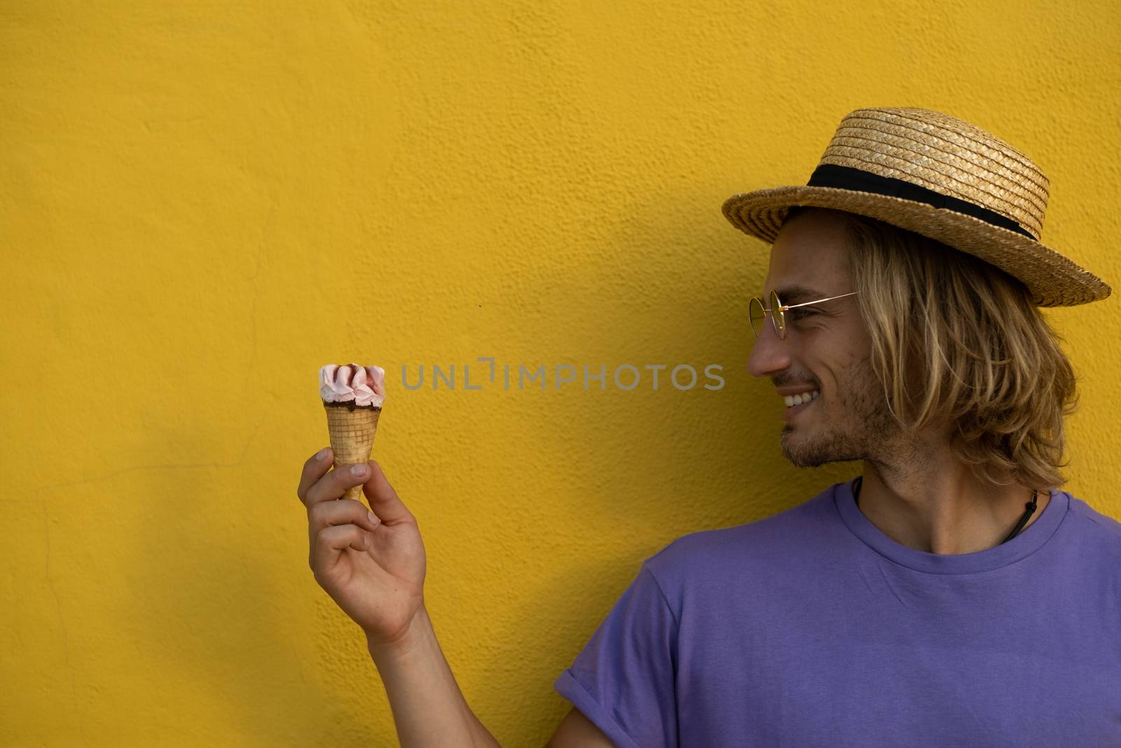 Young blond man with summer clothes, hat and sunglasses enjoying the summer with an ice cream