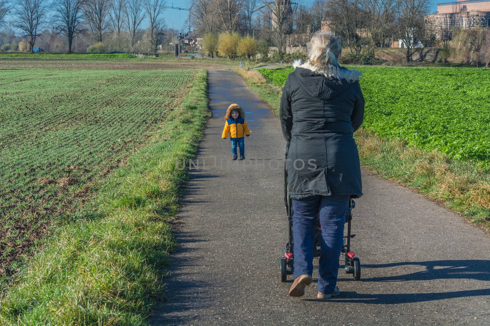 Grandmother with grandson while walking and pushes a baby carriage.