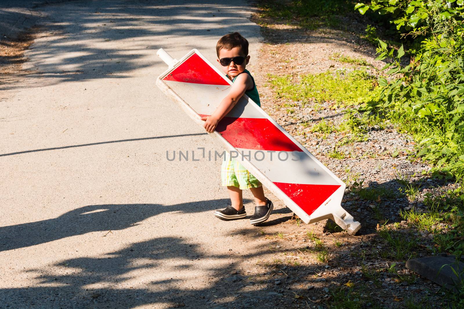 Little boy is carrying a construction site barrier across the street. To overcome difficulties