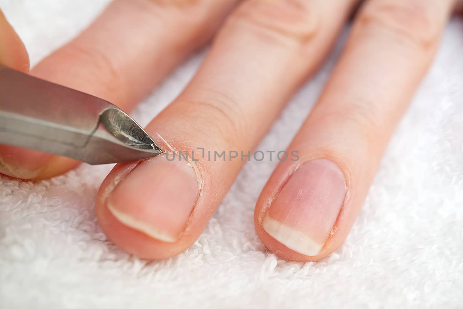 Woman's hand removing nail cuticle on light white table. Care about dry, overgrown cuticle. Closeup. by PhotoTime