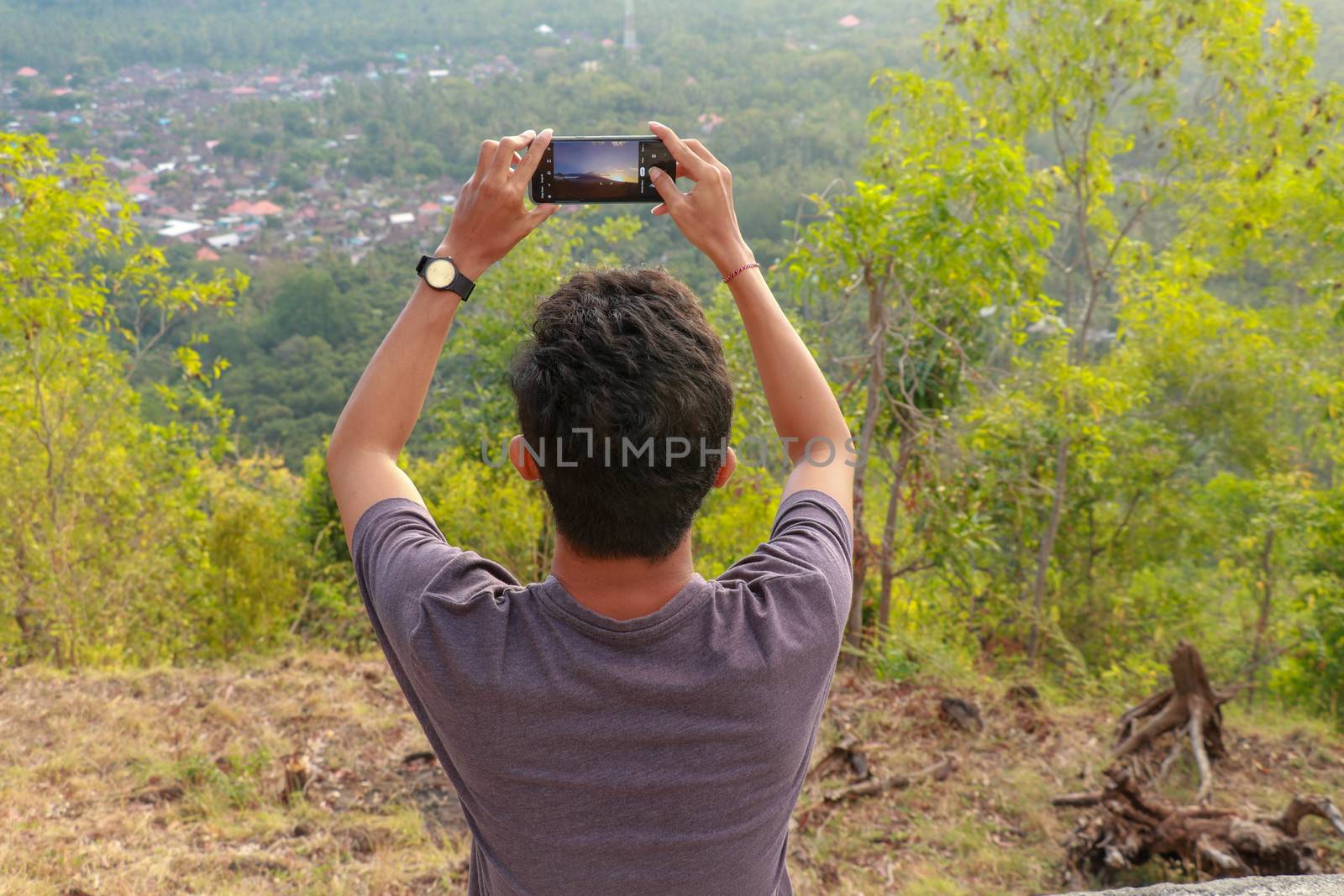 Man photographed mountains in the smartphone. A young man takes pictures of a volcano with a mobile phone. Indonesian teenager photographs during sunset.