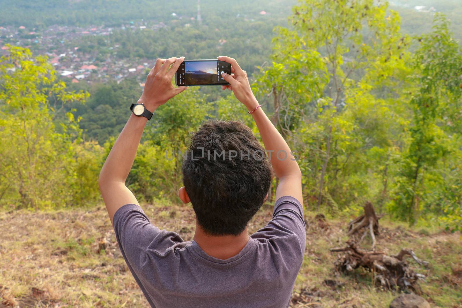 Man photographed mountains in the smartphone. A young man takes pictures of a volcano with a mobile phone. Indonesian teenager photographs during sunset.