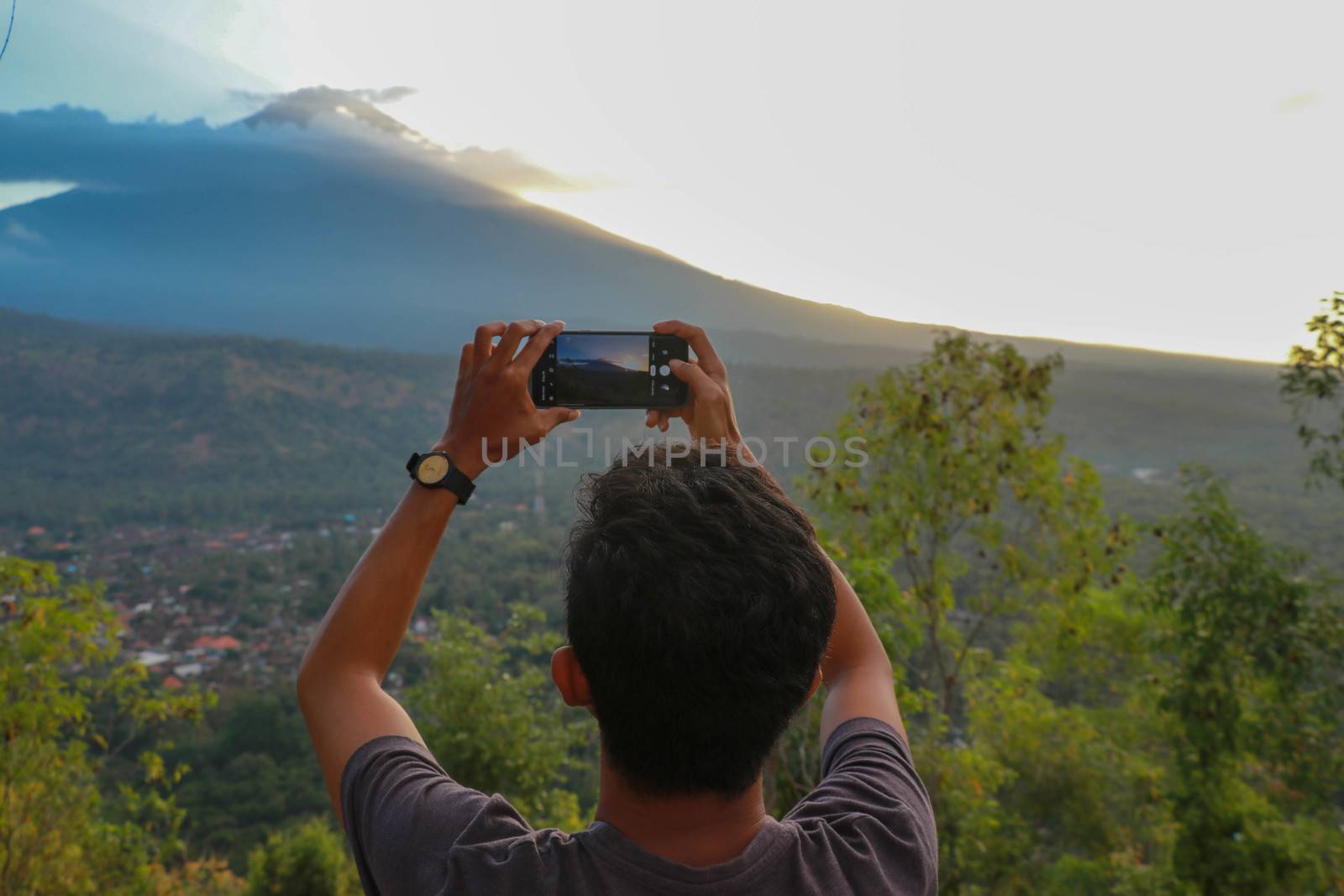 Man photographed mountains in the smartphone. A young man takes pictures of a volcano with a mobile phone. Indonesian teenager photographs during sunset.