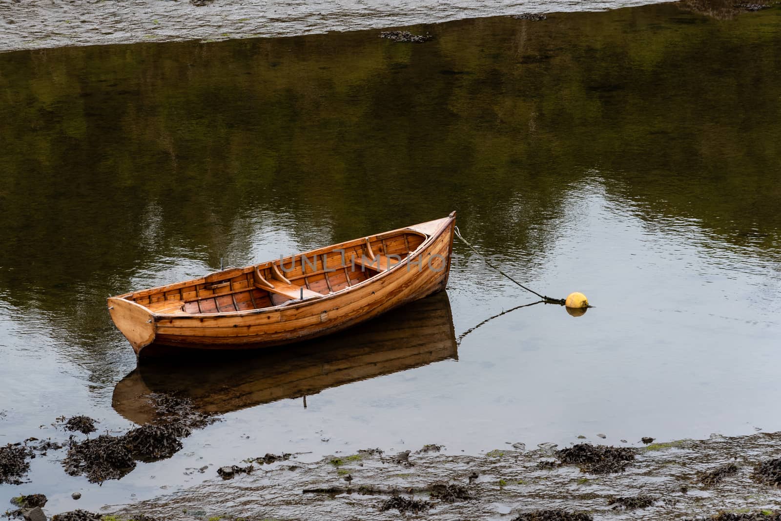 A lone rowboat is anchored in shallow muddy waters.